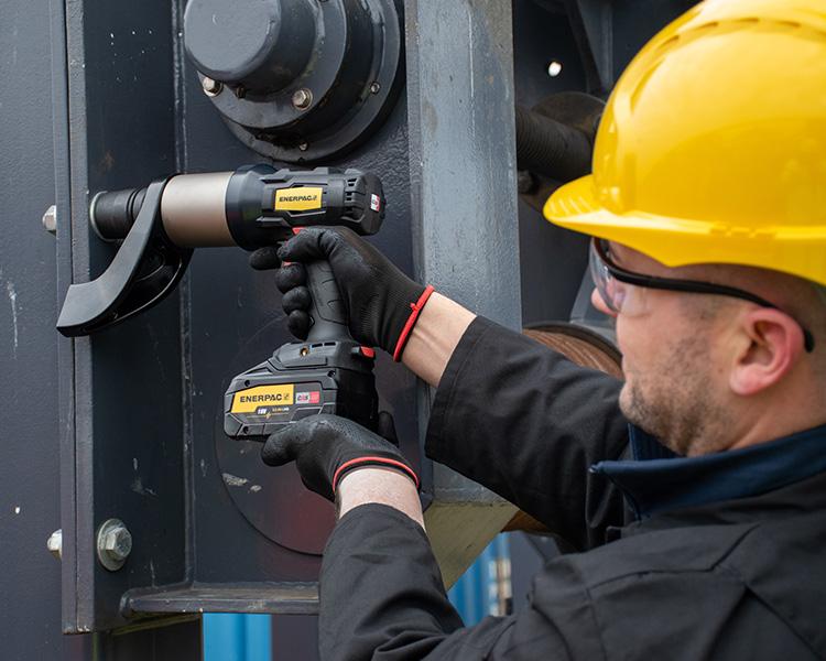 Un travailleur de la construction portant un casque, un gilet de sécurité et une ceinture à outils, se tient fièrement à côté d'un escabeau Featherlite jaune dans un environnement intérieur lumineux.
