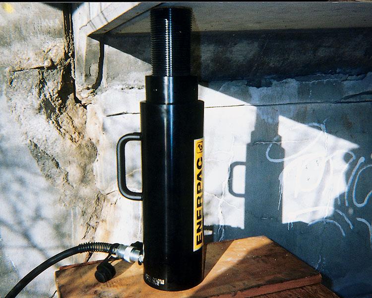 Un travailleur de la construction portant un casque de sécurité, un gilet de sécurité et une ceinture à outils se tient avec confiance à côté d'une échelle Featherlite jaune dans un environnement intérieur lumineux.