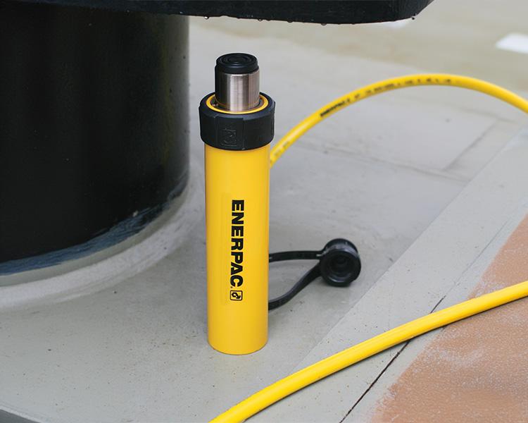 Un travailleur de la construction portant un casque de sécurité, un gilet de sécurité et une ceinture à outils se tient avec confiance à côté d'une échelle Featherlite jaune dans un environnement intérieur lumineux.