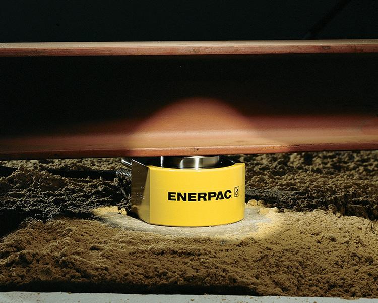 Un travailleur de la construction portant un casque de sécurité, un gilet de sécurité et une ceinture à outils se tient avec confiance à côté d'une échelle Featherlite jaune dans un environnement intérieur lumineux.