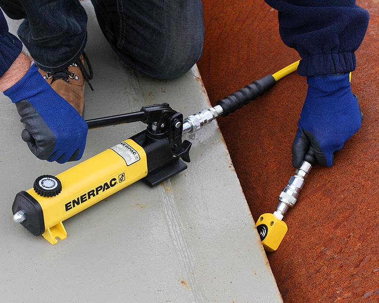 Small enerpac hand pump in a worker'd hand getting ready to fit a small lifting cylinder under some concrete.